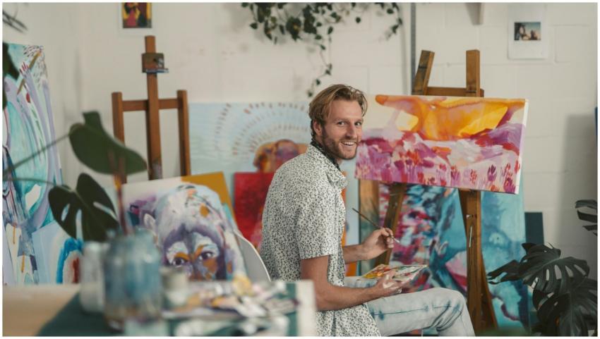 Artist smiling while painting vibrant canvases in
