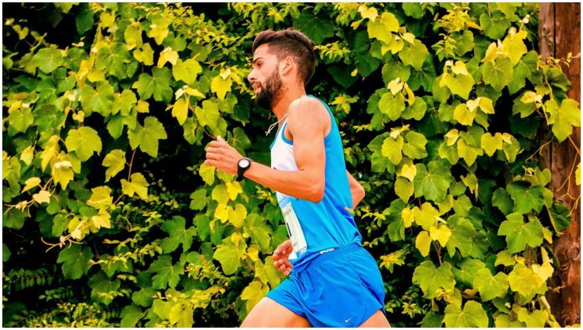 A man jogging outdoors beside vibrant green leaves