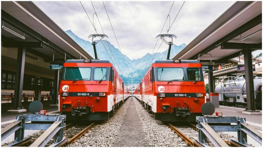 Two red trains at a Swiss station with mountains i
