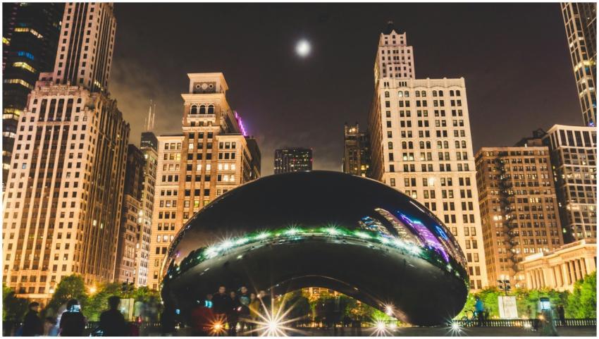Illuminated Cloud Gate with Chicago skyline at nig