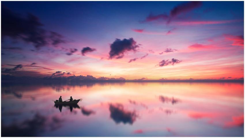 A tranquil sunset scene with a boat silhouetted ag