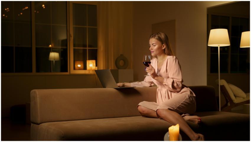 A woman enjoys a glass of wine and uses a laptop w