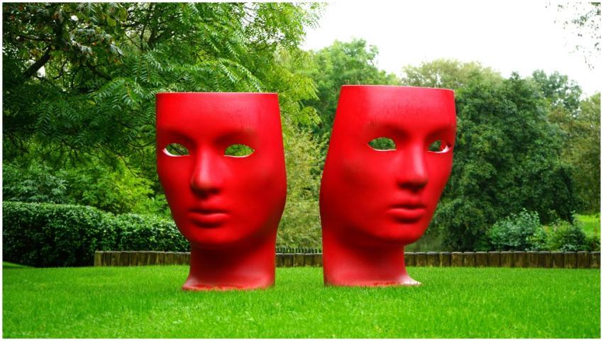 Vivid red mask sculptures in a lush green park set