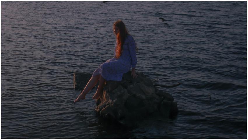 Red-haired woman sitting on rocks by the water at