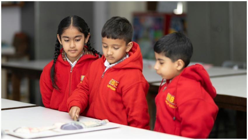 Three children wearing red uniforms engage in a cl