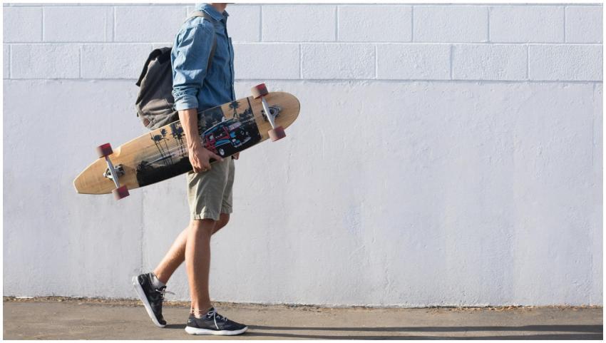 Casual young man walking with longboard against a