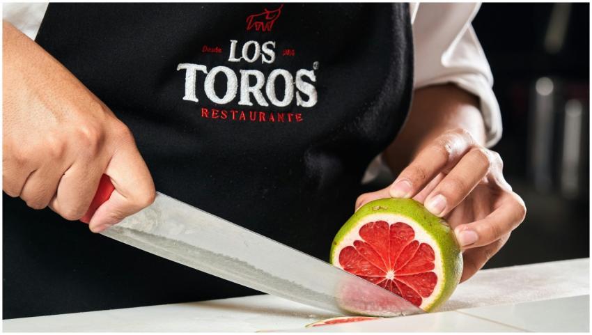 Close-up of chef slicing grapefruit wearing Los To