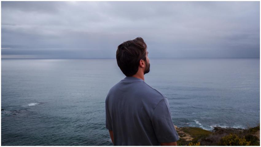 A man stands on a cliff gazing at the peaceful oce