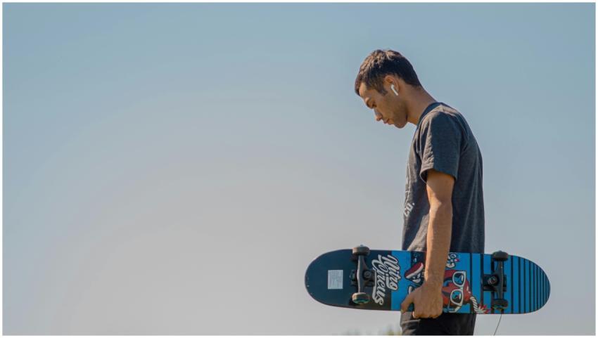 Teenager holding a skateboard, wearing AirPods, un
