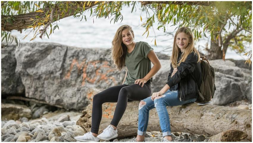 Two smiling teenage girls sitting on a log by the
