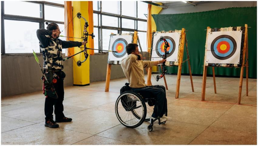 Two adults practicing archery indoors, one in a wh