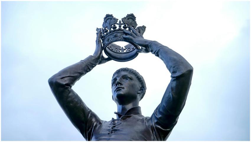 Bronze statue of a figure holding a crown aloft, l