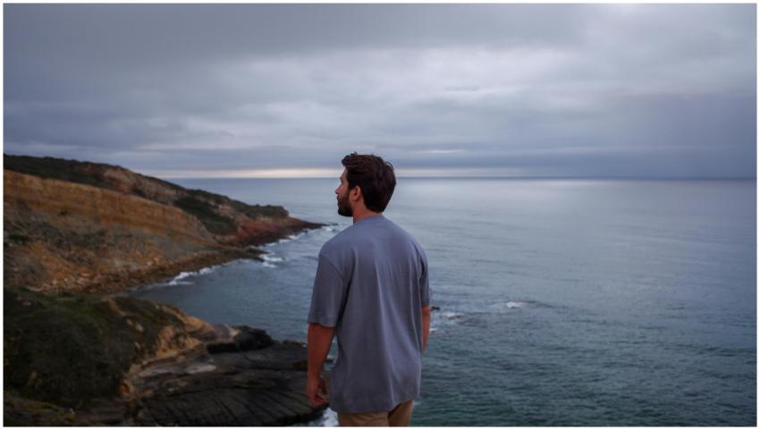 A man standing on a cliff overlooking a calm ocean
