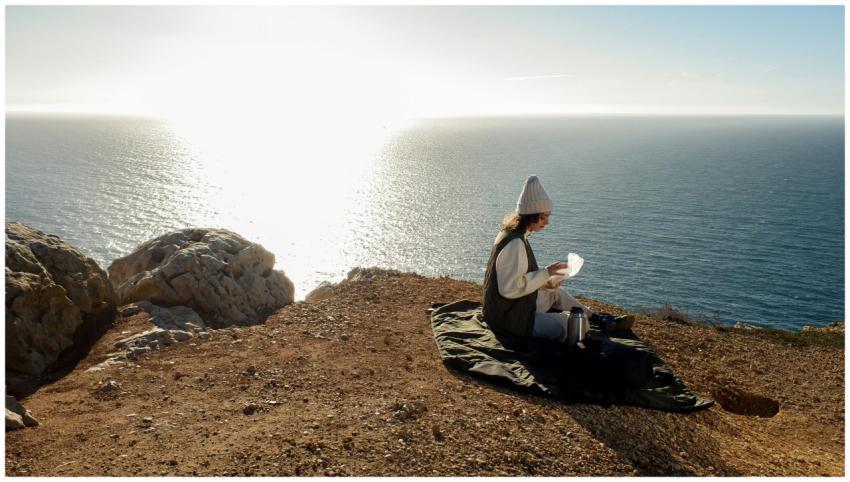 A woman in a beanie sits on a cliffside in Lisbon,