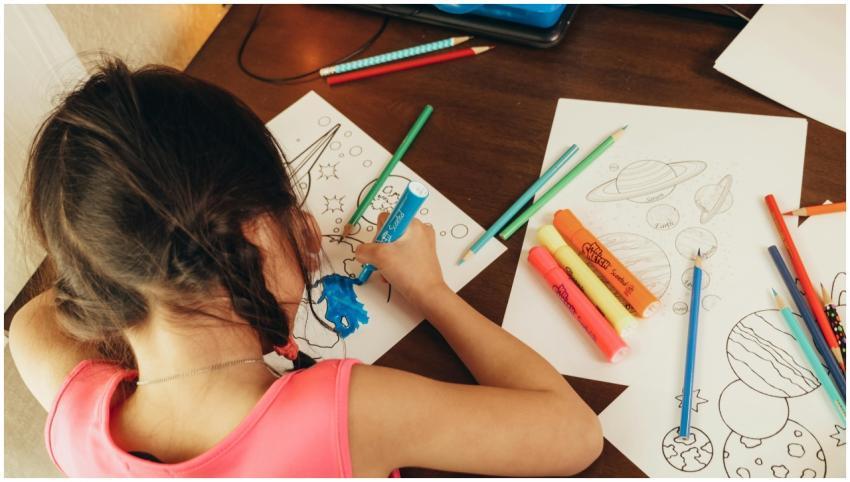Young girl coloring space-themed drawings with mar