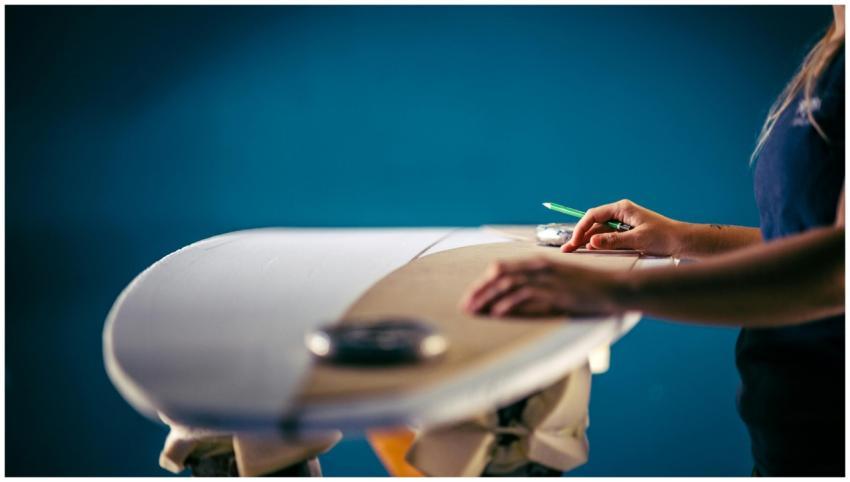 A person carefully shaping a surfboard, focusing o