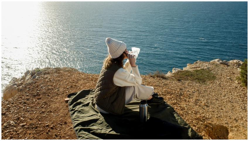 A woman sitting on a cliff edge, enjoying a drink