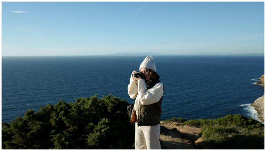A woman in a beanie and puffer vest takes photos b
