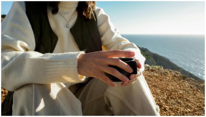 A person sitting outdoors, holding a cup near the
