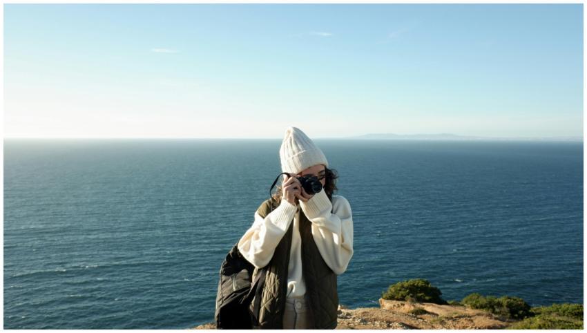 A young woman photographs the ocean from a cliff d