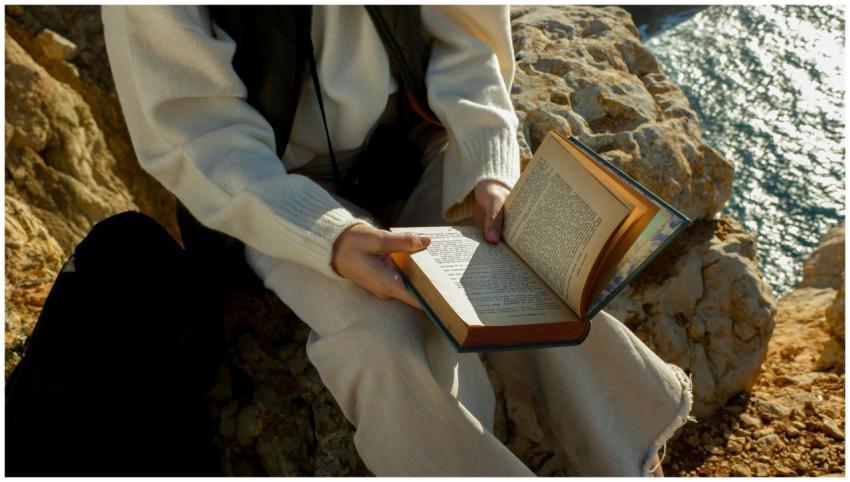 A person reading a book while sitting on a rocky c