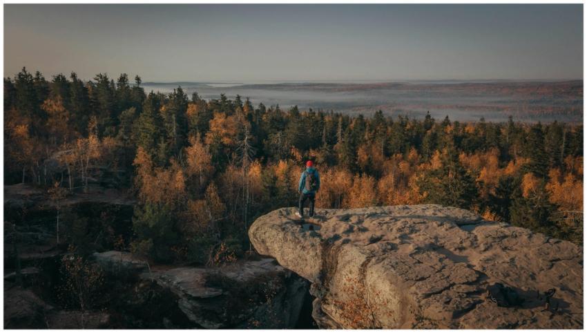 A man in a blue jacket explores the edge of a rock