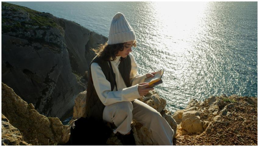 A woman sits on a Sesimbra cliff, reading a book b