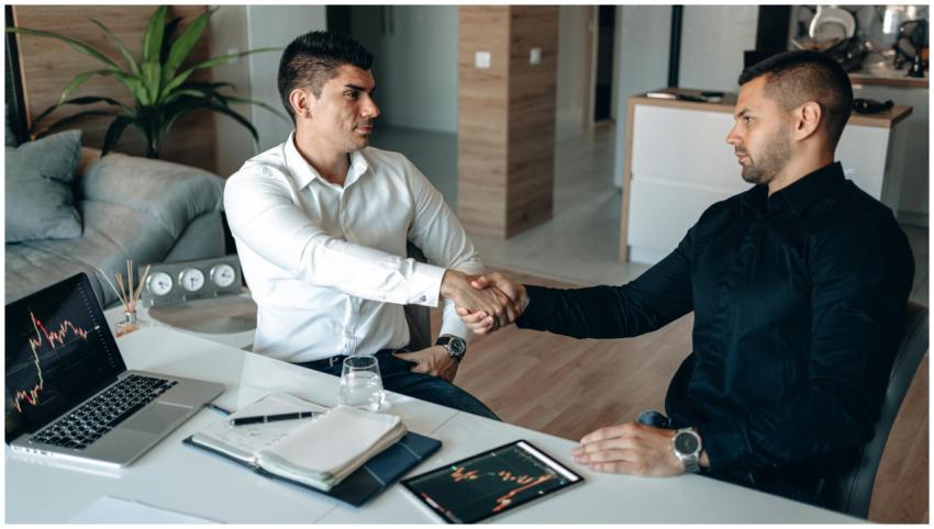 Two businessmen shake hands over financial charts