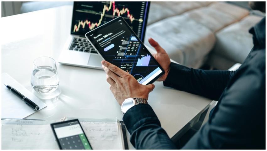 Person holding a tablet showing market data, with
