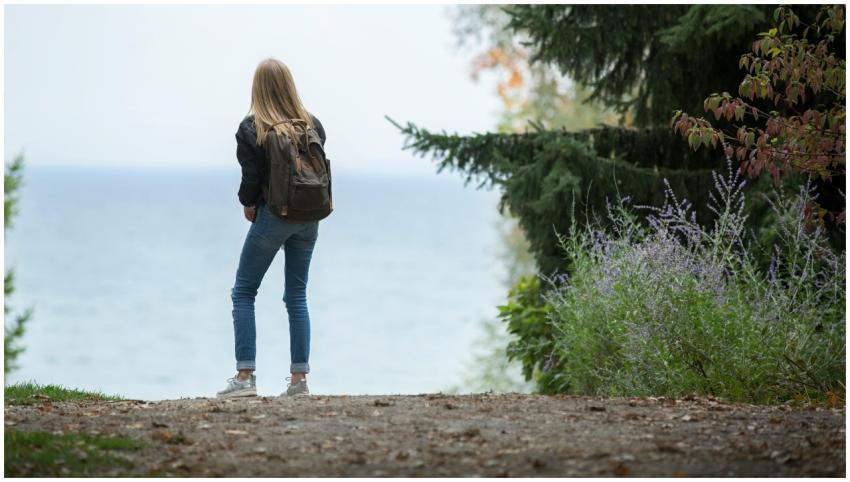 A young woman with a backpack stands on a scenic n