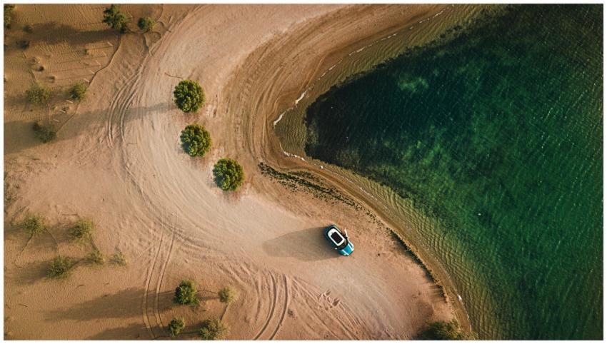 Aerial shot of a sandy beach, water, and parked ca