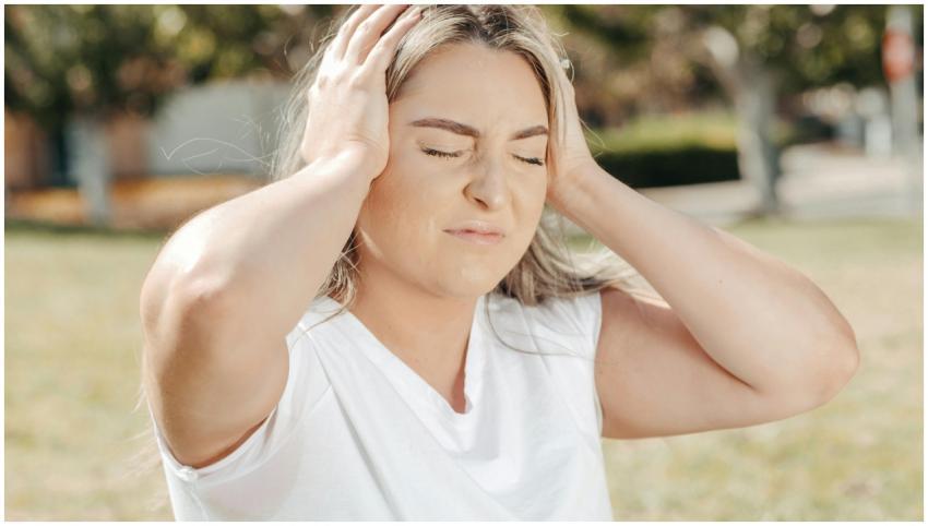 A woman outdoors holds her head, depicting stress