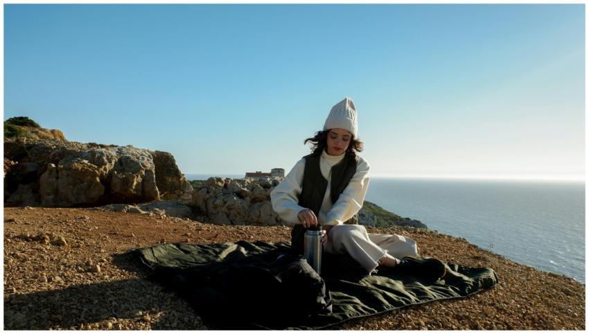 Young woman with thermos enjoys picnic by the ocea