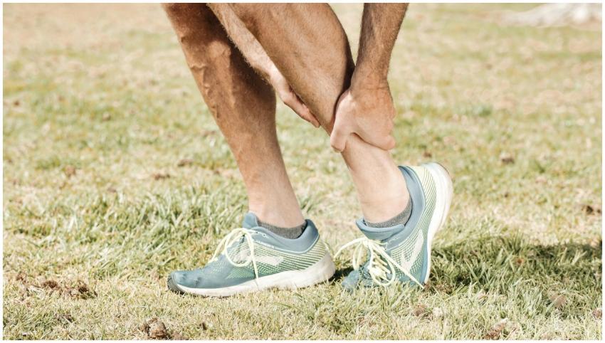 Man holding his calf in pain, wearing teal sneaker