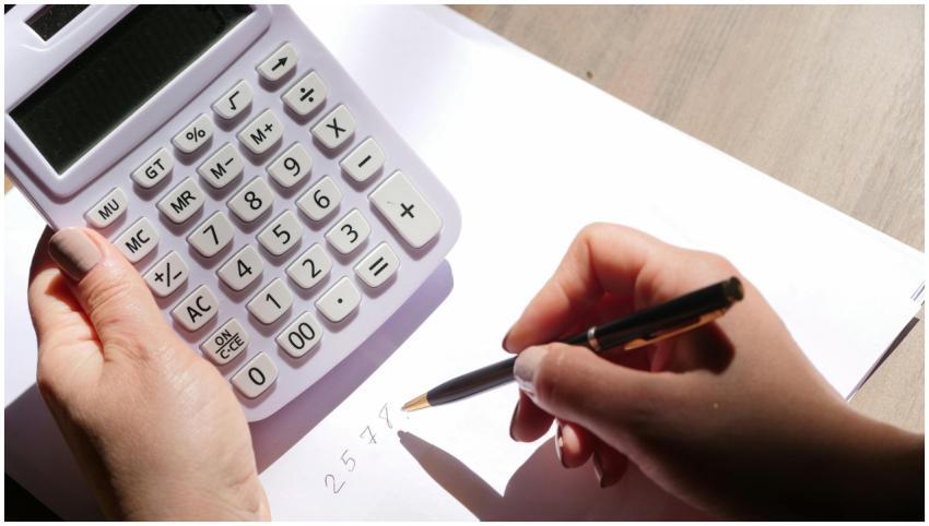 Hands using a calculator and writing numbers on pa