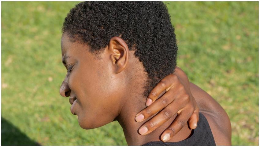 African American woman touching neck outdoors, exp