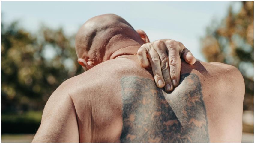 Bald man with tattoo holding back in pain under su