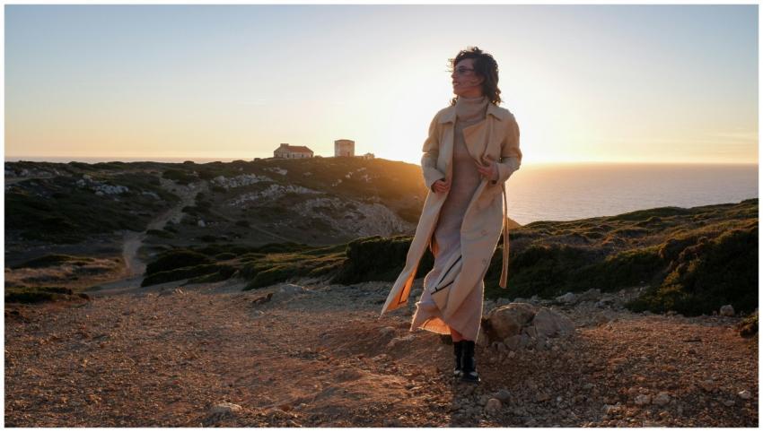 Woman in coat walks on coastal cliff path at sunse