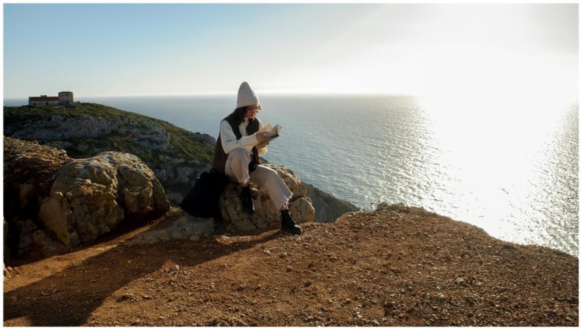 Woman enjoying a book on a scenic cliff with ocean