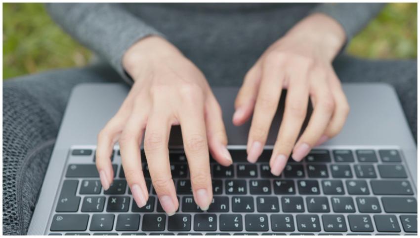 Hands typing on a laptop keyboard in an outdoor se