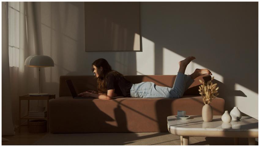 A young woman lying on a sofa using a laptop, enjo