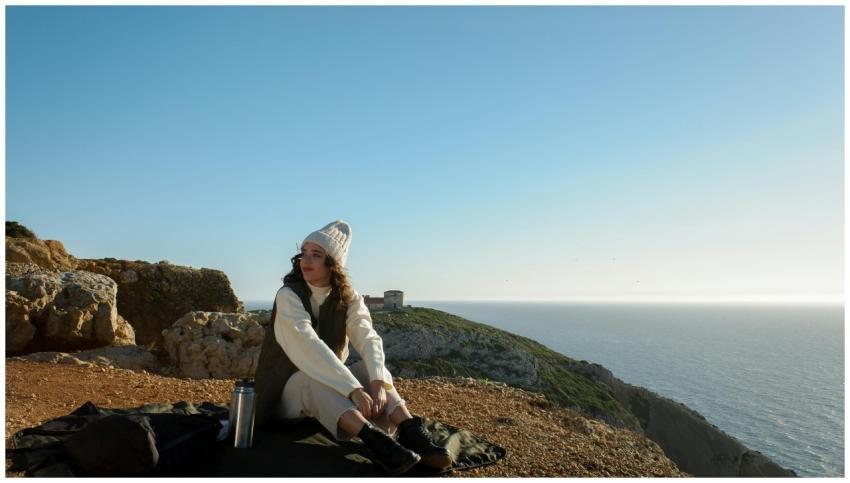 A woman sits by the ocean, embracing the serene cl
