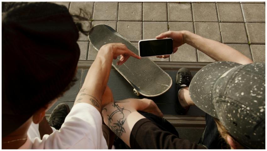 Two teenagers sitting outdoors with a skateboard,