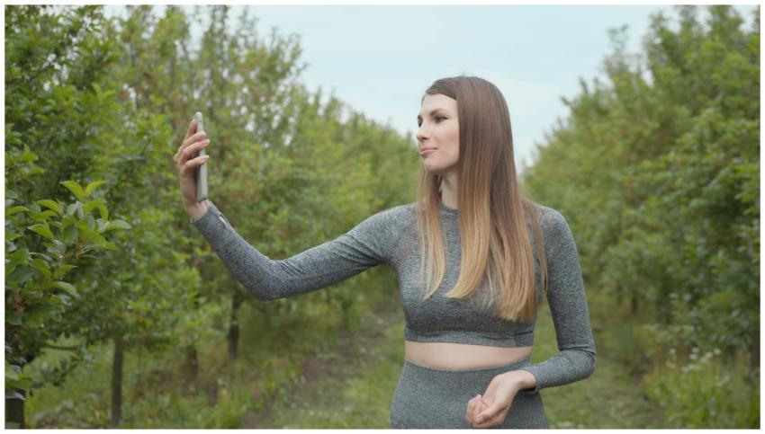 A young woman captures a selfie in a lush orchard,