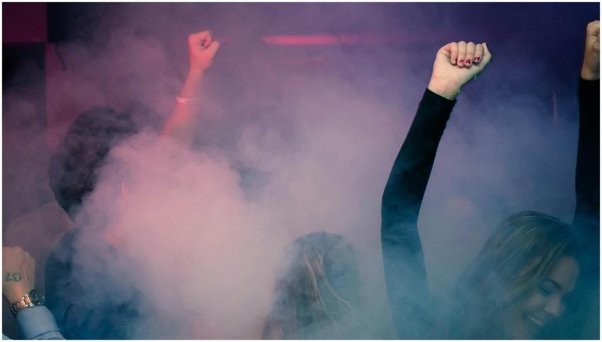 Crowd of people dancing energetically in a foggy n