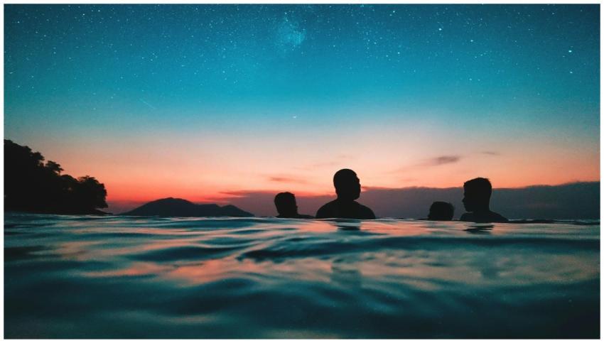 Silhouettes of people in the ocean at sunset under
