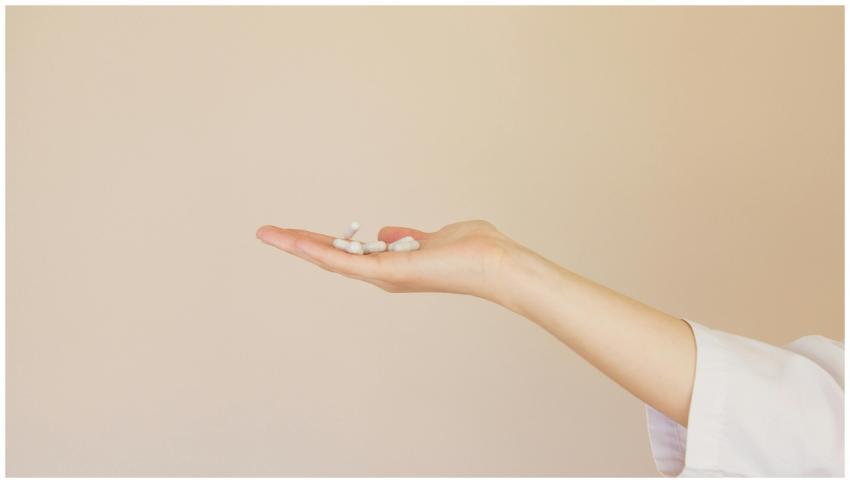 A female hand in a lab coat holds white capsules a