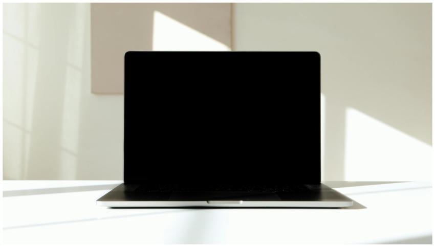 A modern laptop with a black screen on a sunlit wh