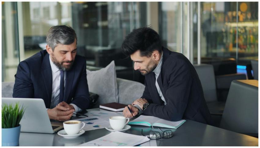 Two businessmen discussing charts over coffee at a