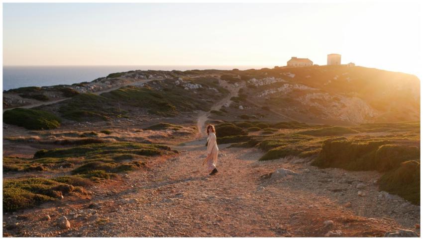 A woman strolls on a rocky coastal path during sun